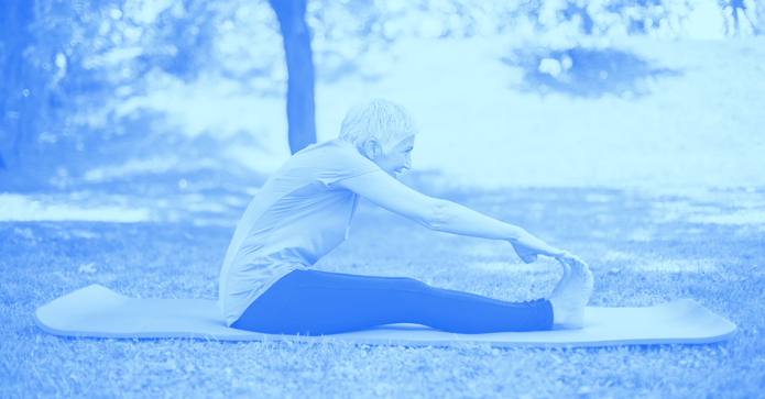 Elderly person touching their toes on a yoga mat outside.